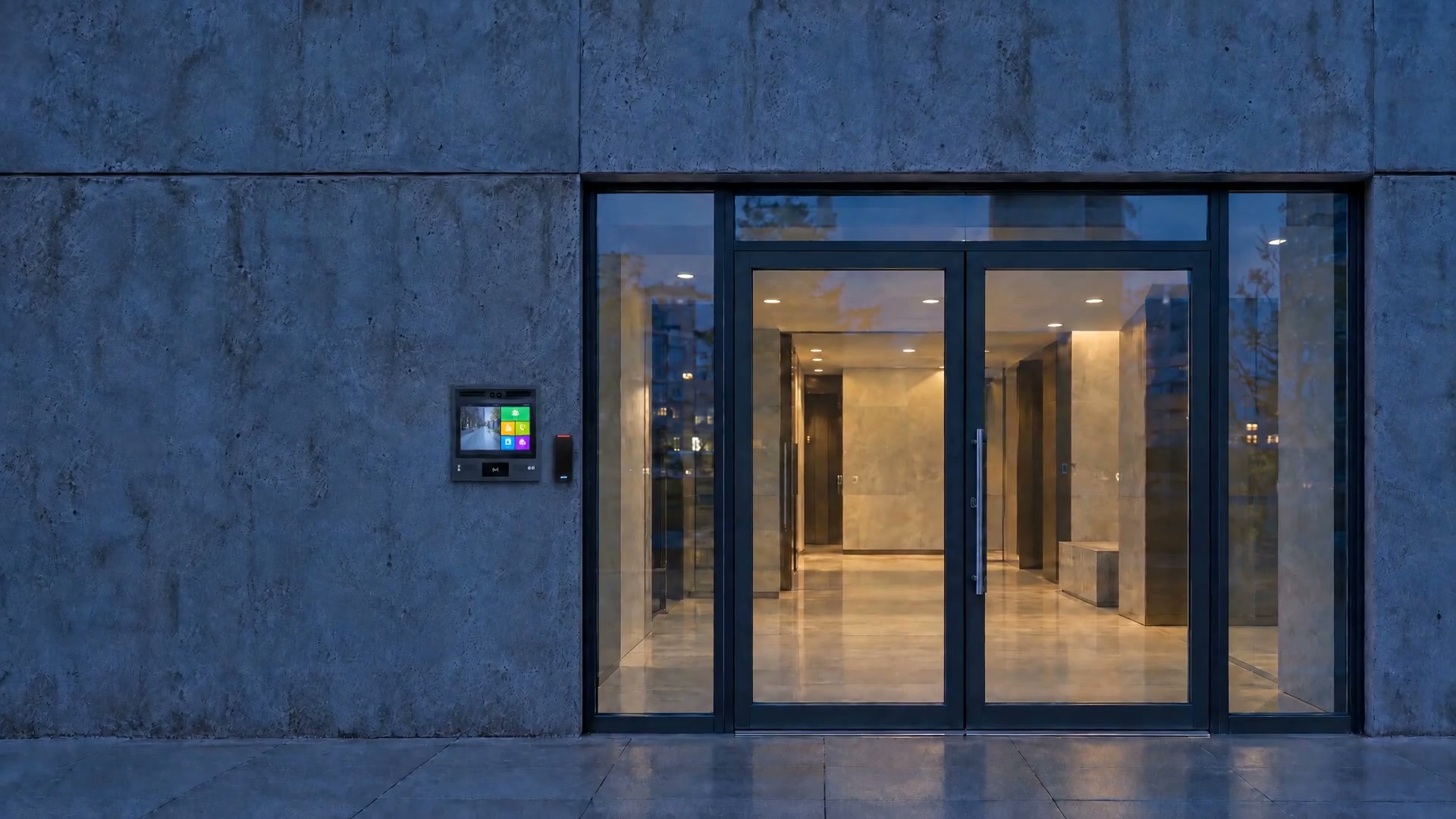A building entrance at dusk with a touchscreen door station and a card reader beside the glass doors