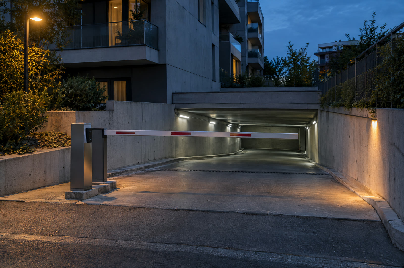 A parking garage entrance at dusk with an automatic barrier arm and a card reader pedestal